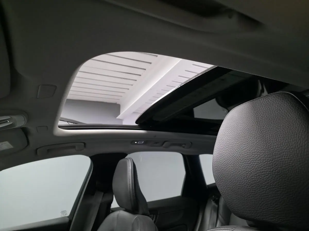 Vue intérieure du toit ouvrant panoramique ouvert et sièges avant en cuir noir du Volvo XC60 gris 2023.