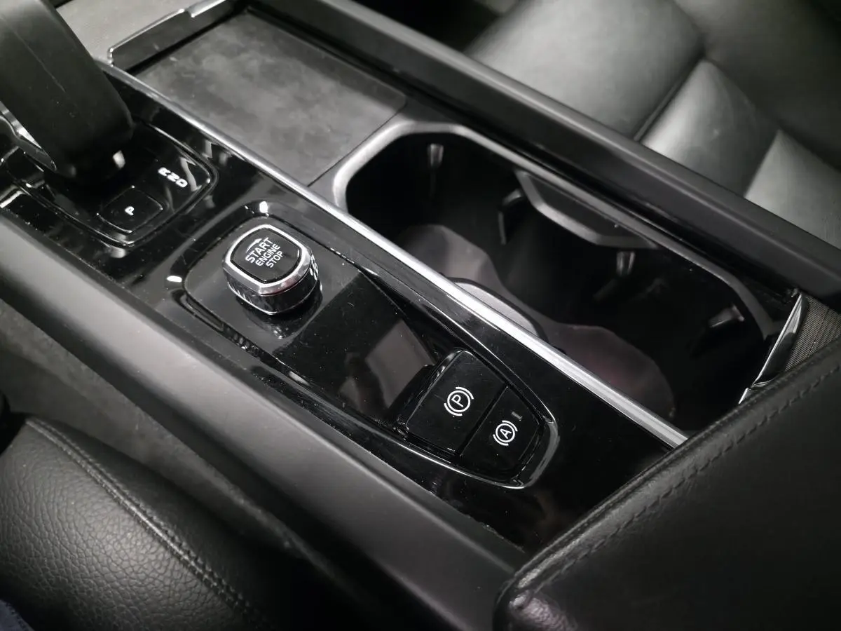 Gros plan sur la console centrale noire brillante du Volvo XC60 2023 avec bouton Start/Stop et commandes de frein à main.
