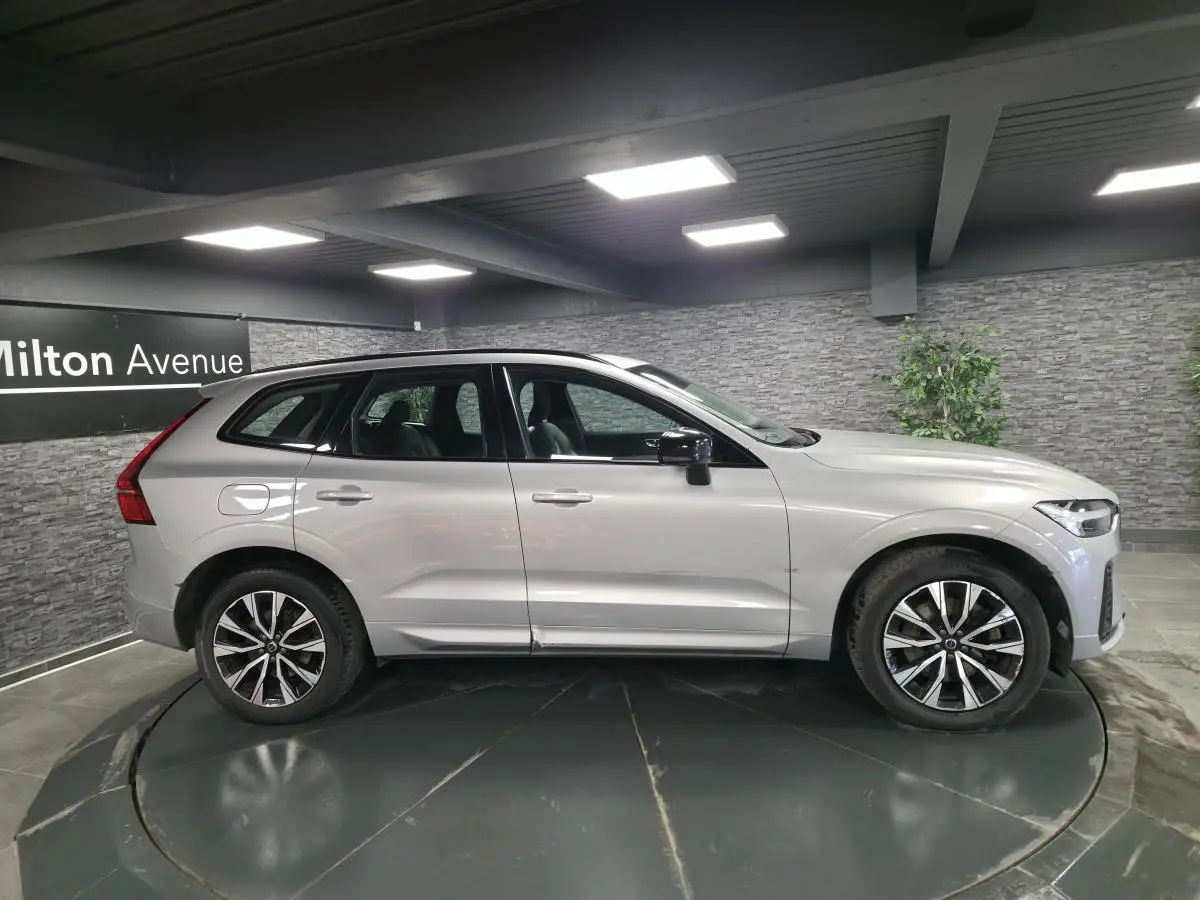 Vue latérale gauche d'un Volvo XC60 gris métallisé 2023 avec jantes alliage 19 pouces et toit ouvrant panoramique.