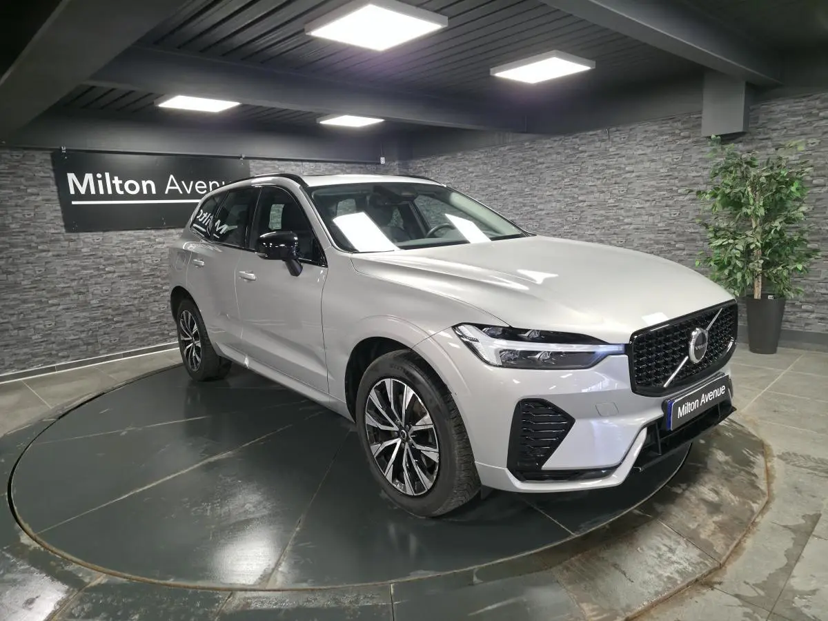 Volvo XC60 gris métallisé en 3/4 avant droit, avec calandre et jantes noires dans un showroom.