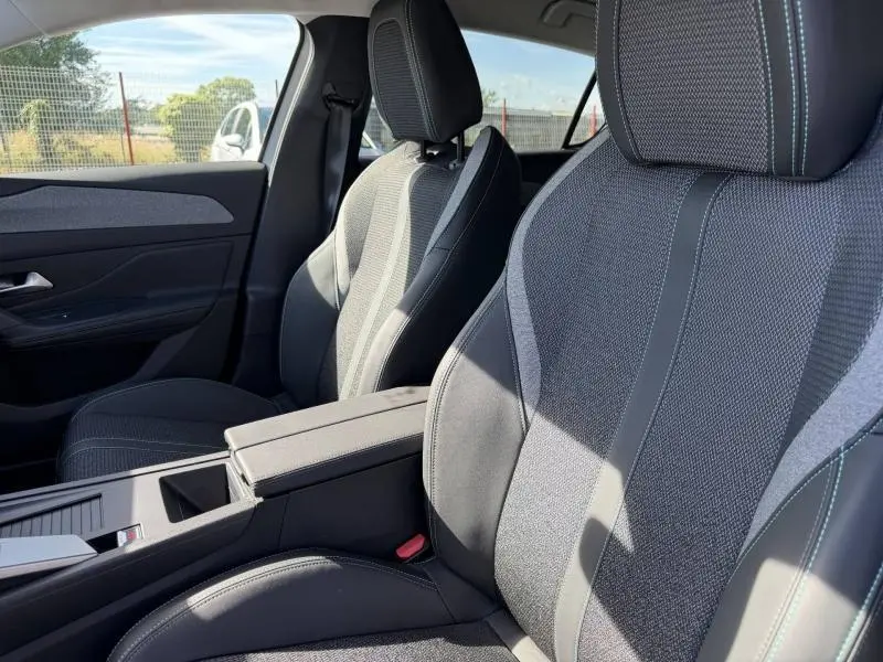 Vue intérieure côté droit montrant les sièges avant en tissu gris et accoudoir central de la Peugeot 308 Hybrid 2025.