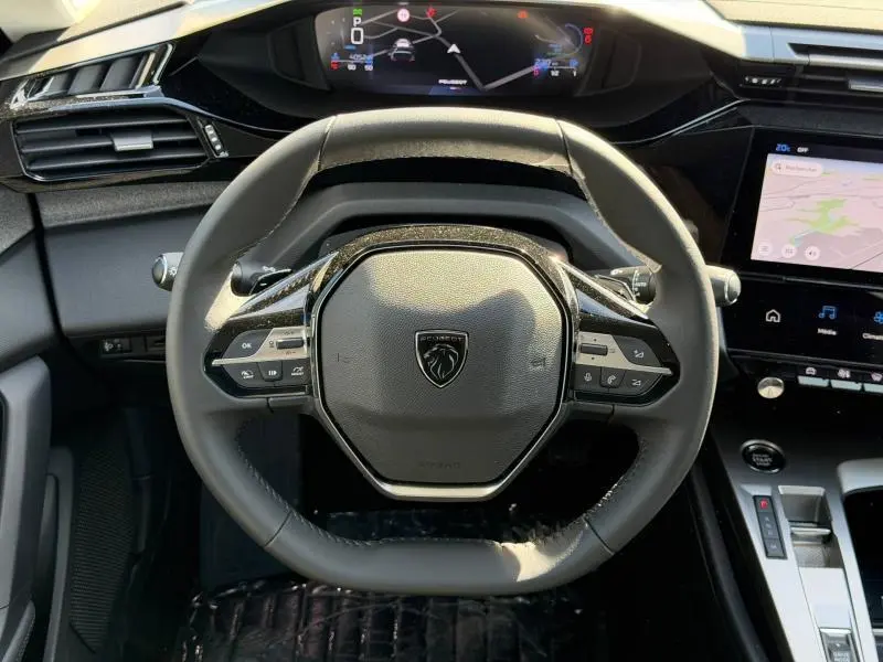 Vue intérieure centrée sur le volant multifonction noir du Peugeot 308 Hybrid 2025 avec tableau de bord numérique et écran tactile.