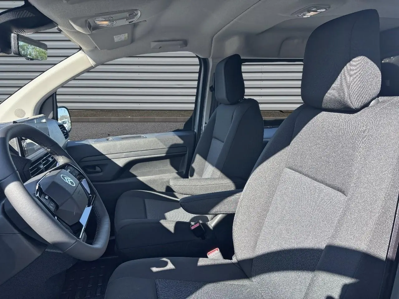Vue intérieure côté conducteur du Citroën Jumpy gris, montrant les sièges avant et le volant en cuir.