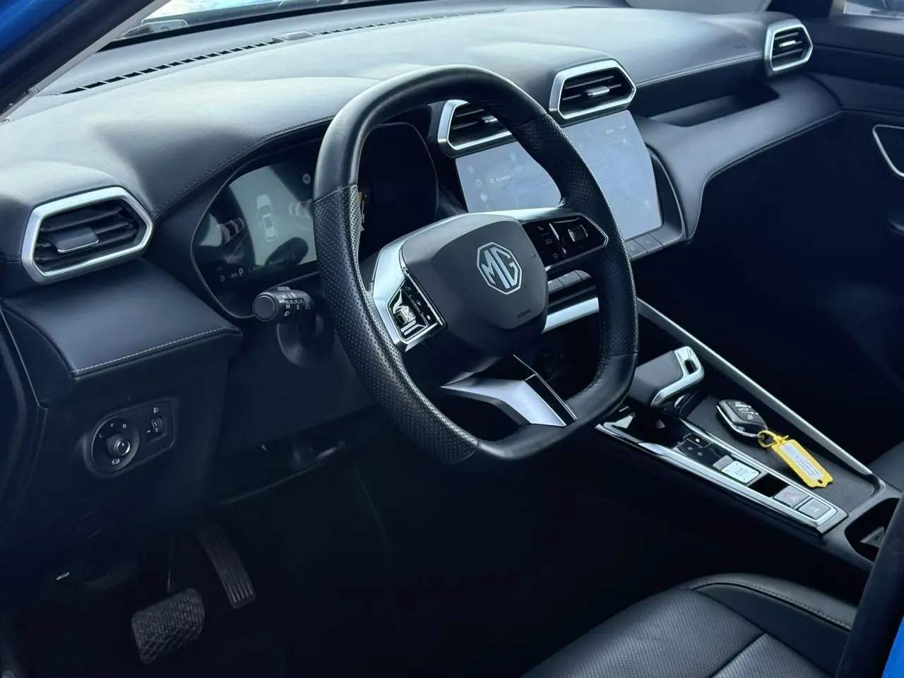 Vue intérieure côté conducteur du MG ZS 1.5 Hybrid+ 197 Luxury, avec volant cuir noir et écran tactile central.