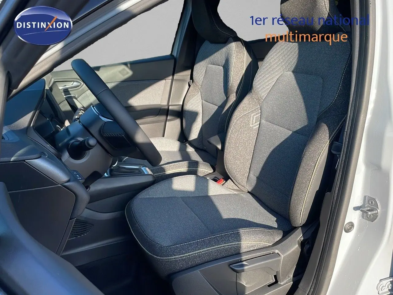 Vue intérieure côté conducteur du Renault Captur 2025, sièges tissu gris avec logo Renault brodé sur dossier.