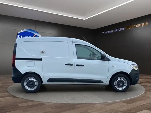 Profil droit du Renault Express Van blanc 2023 avec porte coulissante et jantes tôlées noires sur fond intérieur showroom.
