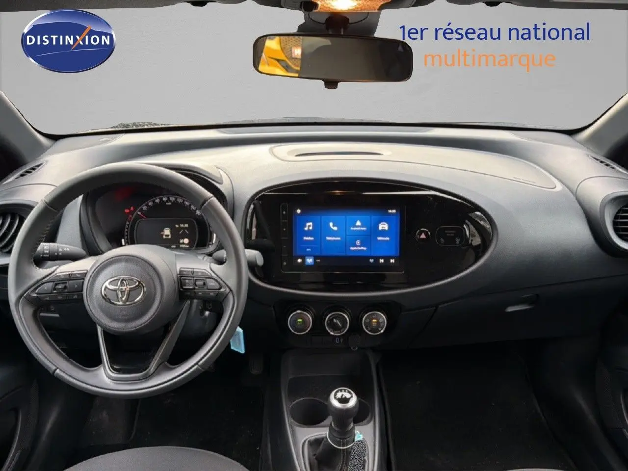 Vue intérieure frontale du tableau de bord noir de la Toyota Aygo X 2025 avec écran tactile et boîte manuelle.