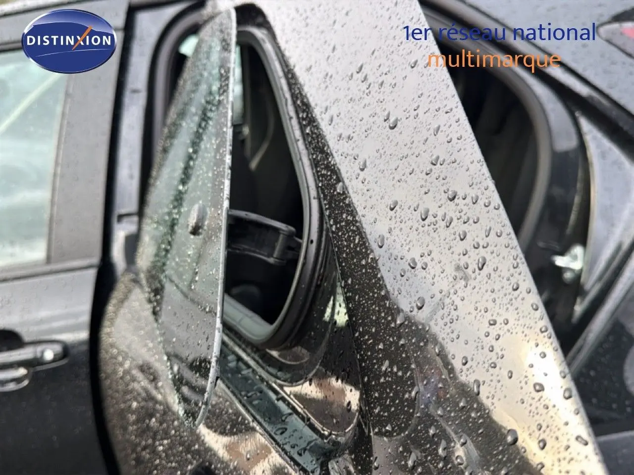 Gros plan sur le rétroviseur côté gauche d'une Toyota Aygo X noire 2025, avec gouttes de pluie visibles sur la carrosserie.