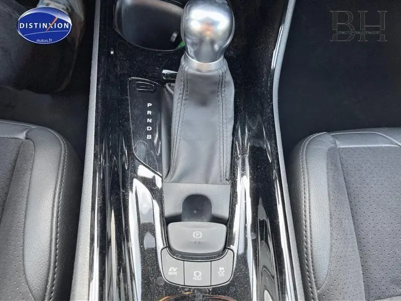 Vue rapprochée de la console centrale noire brillante avec levier de vitesse et boutons de commande du Toyota C-HR blanc nacré.