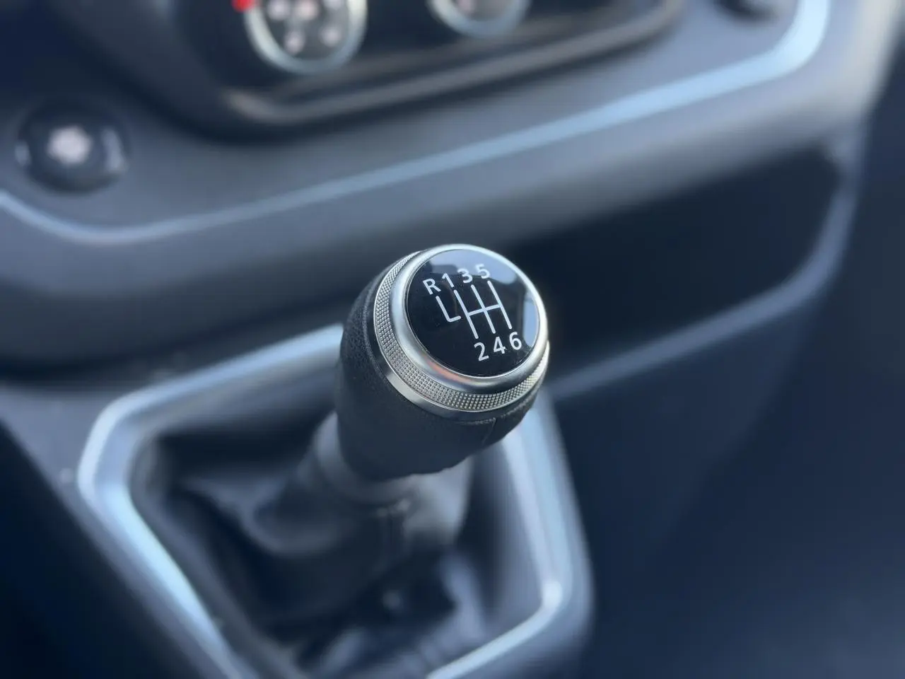 Gros plan sur le levier de vitesses manuel noir du Nissan Primastar gris, avec marquages blancs des rapports visibles.
