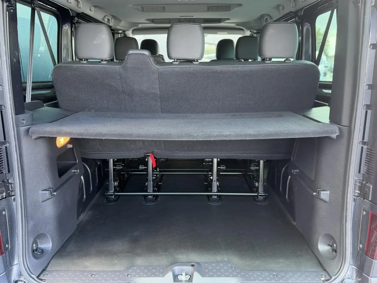 Coffre ouvert d’un Nissan Primastar gris Comète, vue arrière montrant les sièges arrière et la tablette de séparation.
