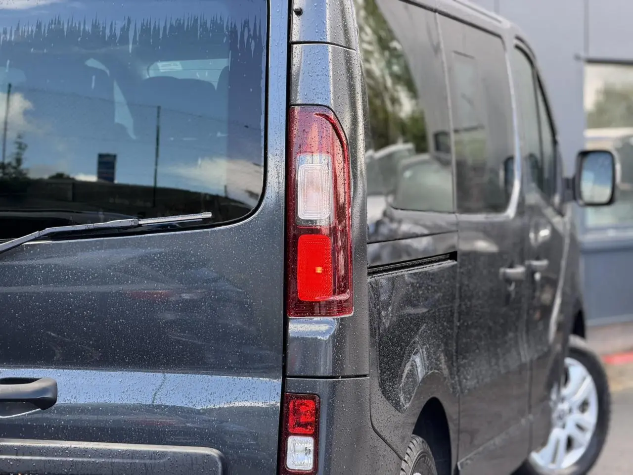 Vue arrière gauche rapprochée du Nissan Primastar gris comète avec hayon vitré et feux arrière allongés.