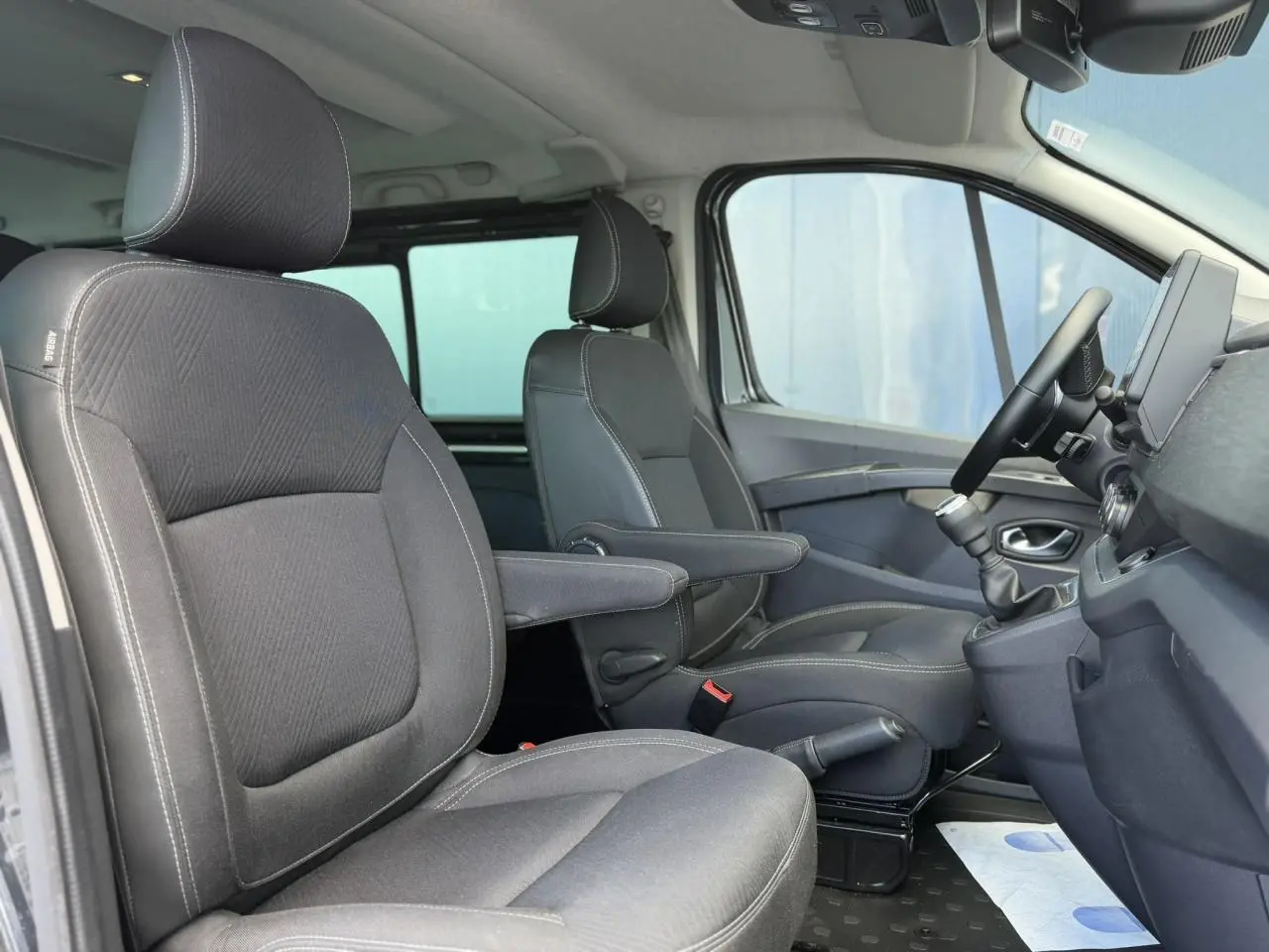 Vue intérieure côté droit du Nissan Primastar 2025, montrant les sièges avant gris foncé avec accoudoirs et tableau de bord.