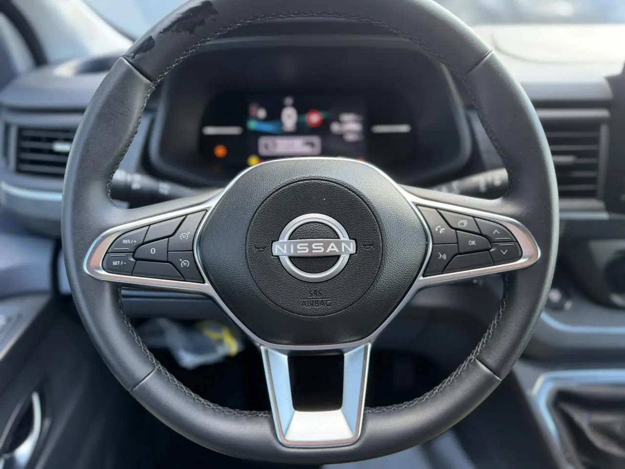 Vue rapprochée du volant noir du Nissan Primastar 2025 avec commandes intégrées et logo central argenté.