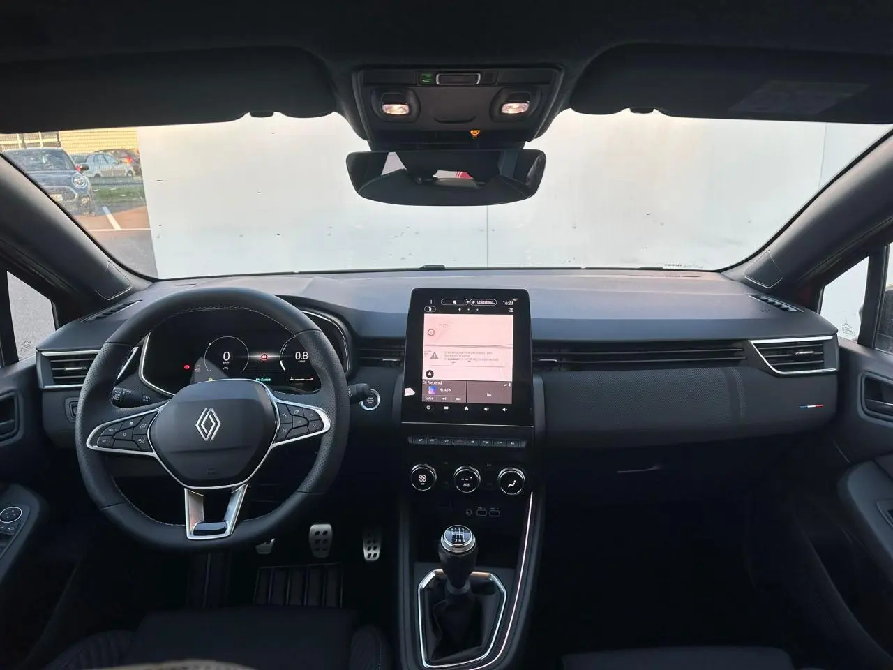 Vue intérieure frontale du tableau de bord de la Renault Clio V rouge foncé, avec volant multifonction et écran tactile vertical.