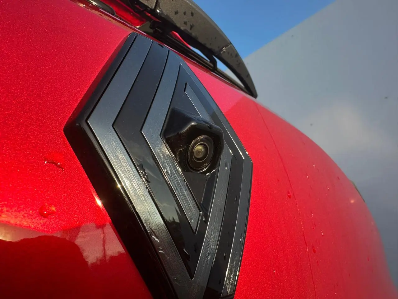 Gros plan sur le logo Renault noir brillant avec caméra intégrée sur la calandre rouge foncé de la Clio V Alpine.
