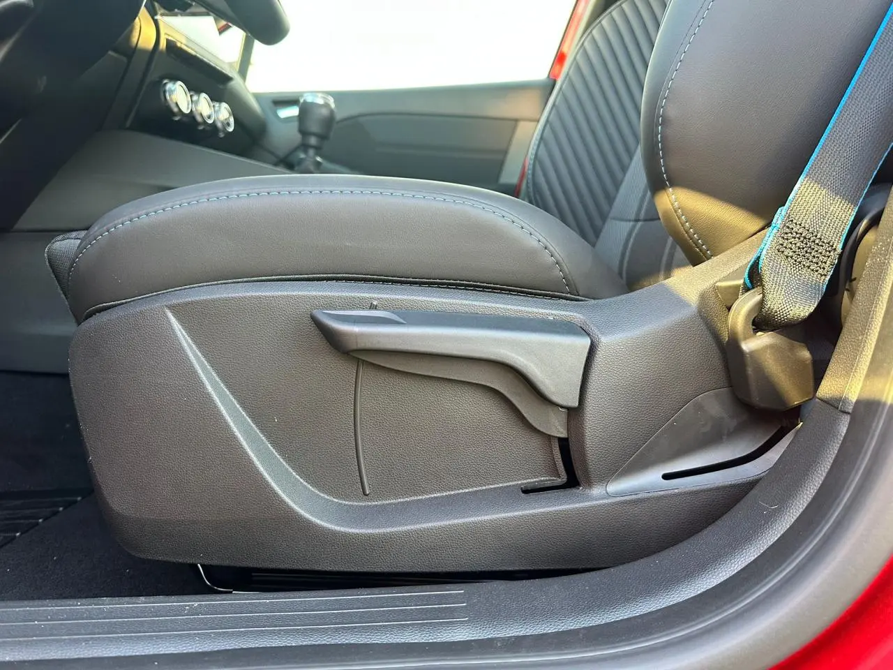 Détail de l'accoudoir avant coulissant côté gauche avec sellerie noire et surpiqûres bleues sur Renault Clio rouge foncé.