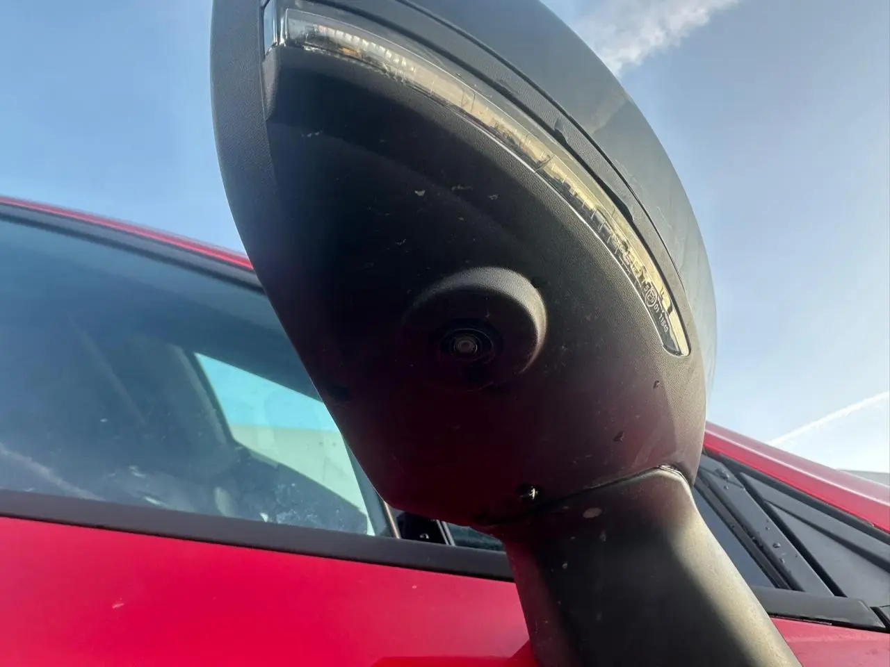 Gros plan sur le rétroviseur droit noir brillant avec caméra, sur Renault Clio rouge foncé vue côté droit.
