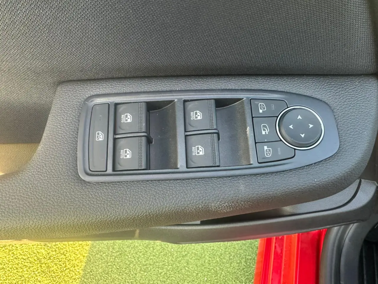 Détail des commandes des vitres et rétroviseurs sur la porte côté conducteur d’une Renault Clio rouge foncé.