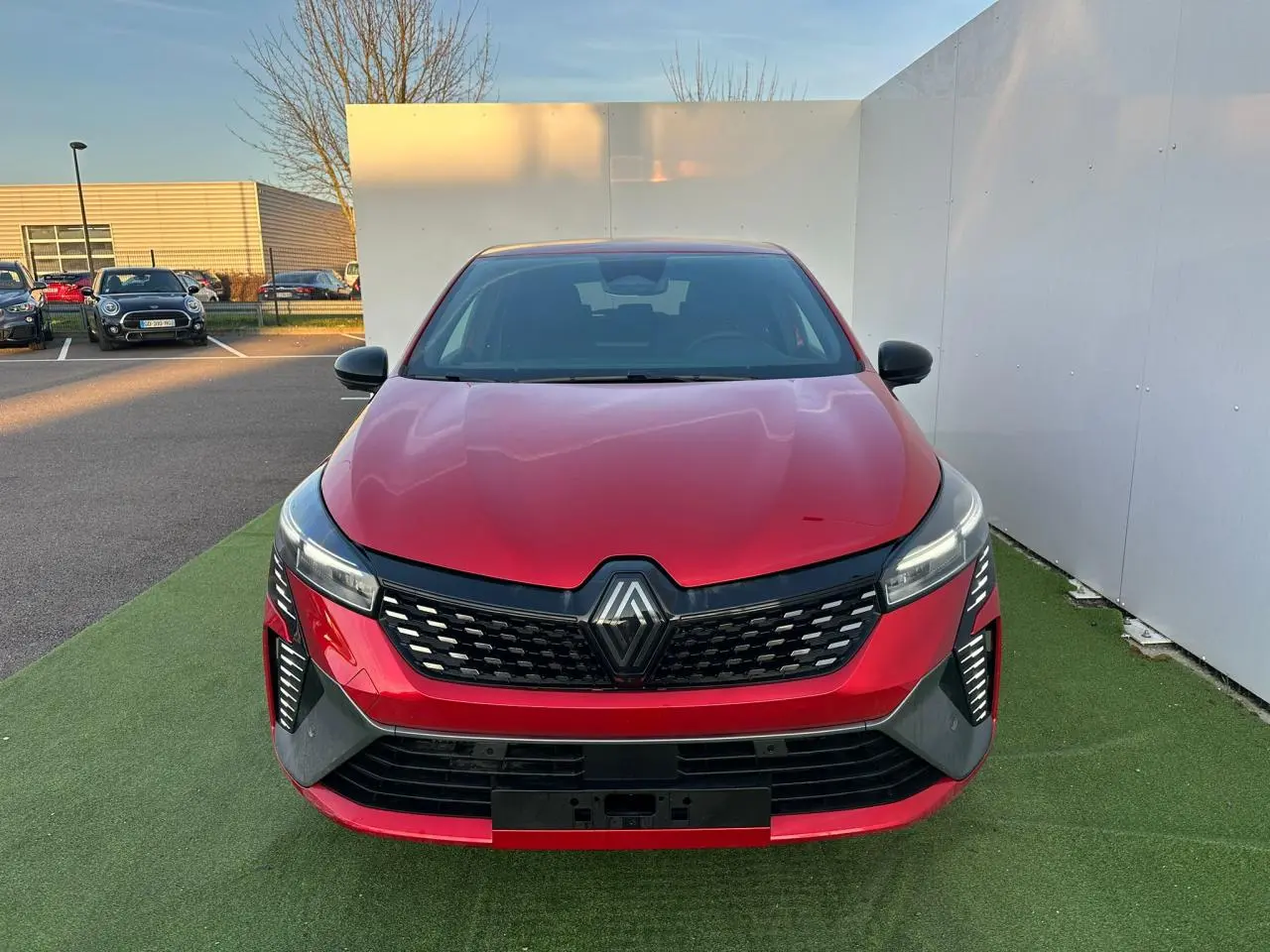 Vue frontale d'une Renault Clio rouge foncé avec calandre noire et feux LED en signature lumineuse verticale.