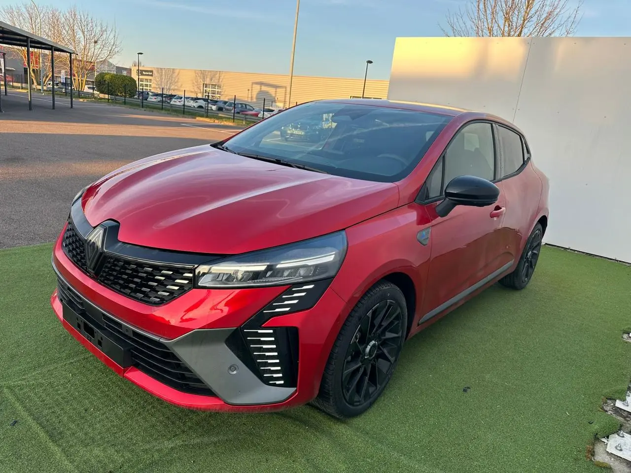 Renault Clio 2025 rouge foncé vue 3/4 avant droit avec calandre noire et jantes alliage noires.