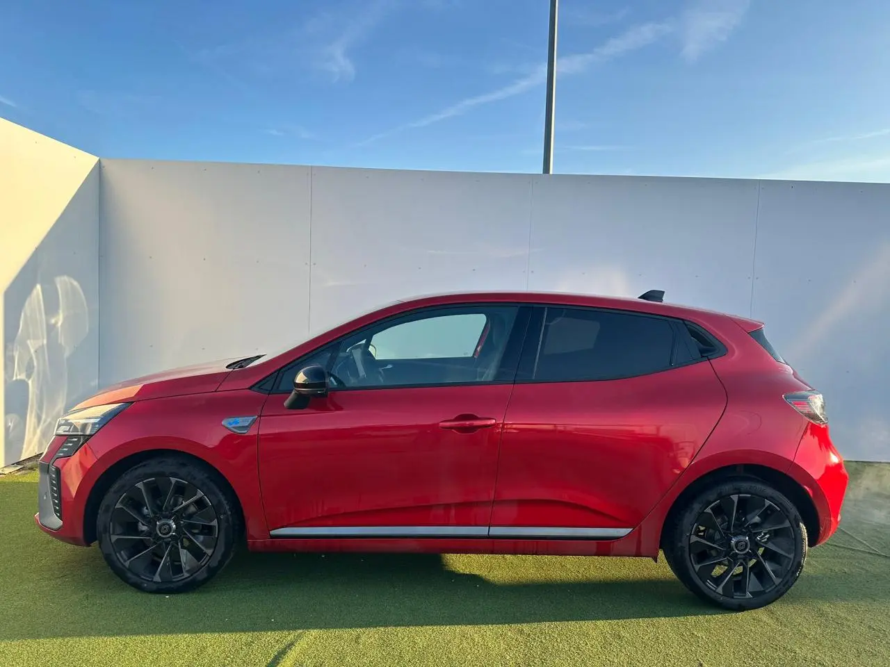 Profil droit de la Renault Clio V rouge foncé avec jantes noires et badges esprit Alpine visibles sur ailes avant.