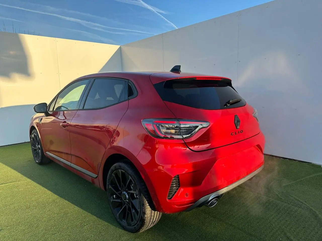 Vue 3/4 arrière droite d'une Renault Clio rouge foncé avec jantes noires et badges Alpine sur fond clair.