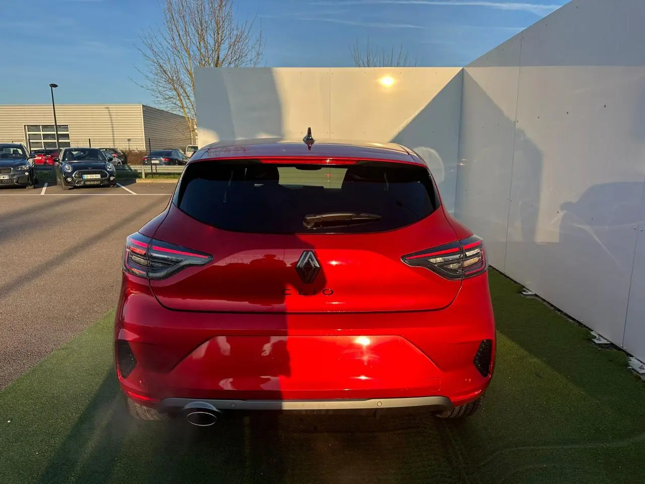 Vue arrière d'une Renault Clio rouge foncé 2025 avec feux arrière LED en forme de C et antenne requin noire.