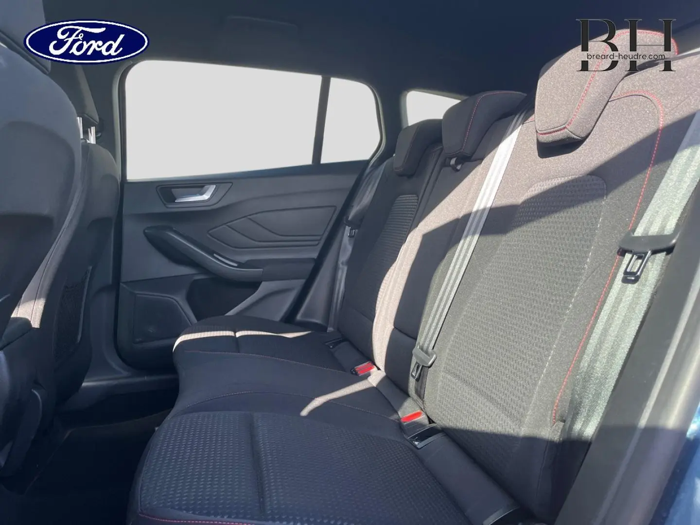 Vue latérale droite de l’intérieur arrière de la Ford Focus SW 2024 avec sièges tissu noir et surpiqûres rouges.