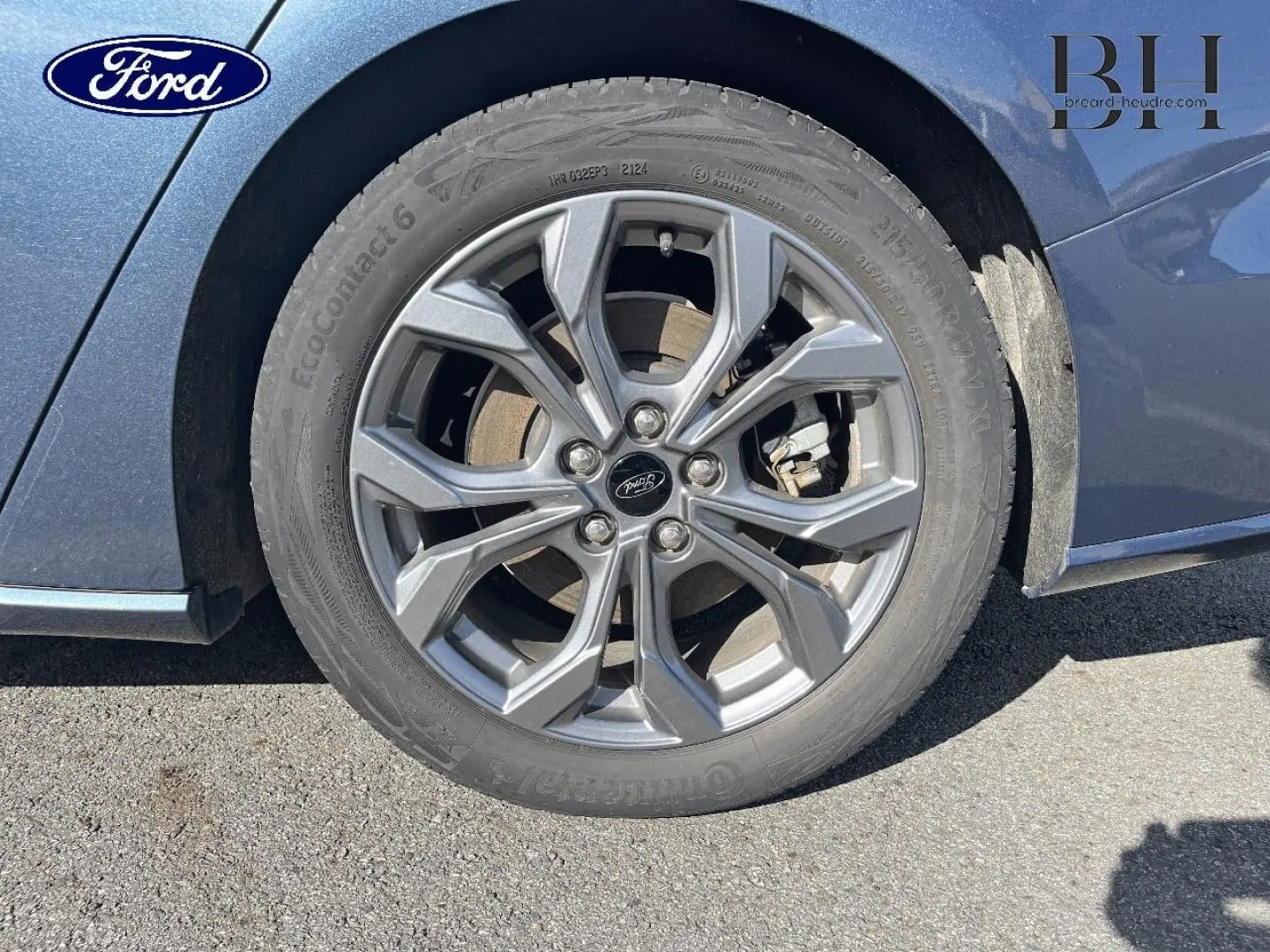 Gros plan sur la roue avant gauche avec jante alu grise du Ford Focus SW bleu azur métallisé 2024.