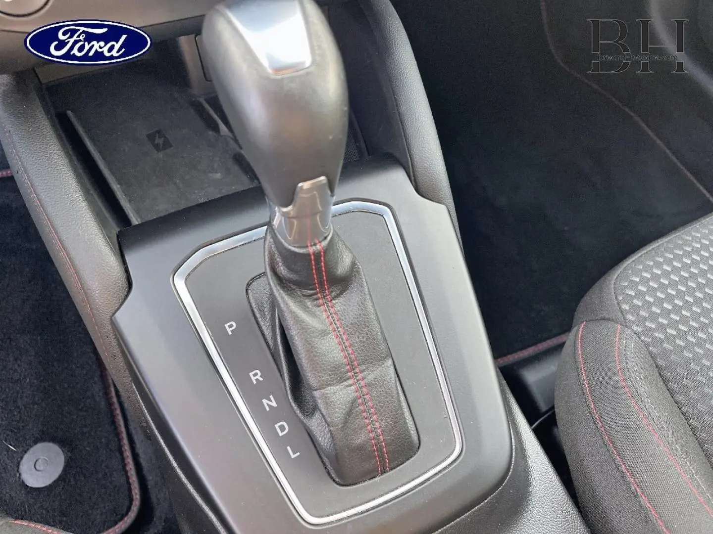 Gros plan sur le levier de vitesses automatique avec surpiqûres rouges, console centrale et siège tissu noir à surpiqûres rouges Ford Focus SW.
