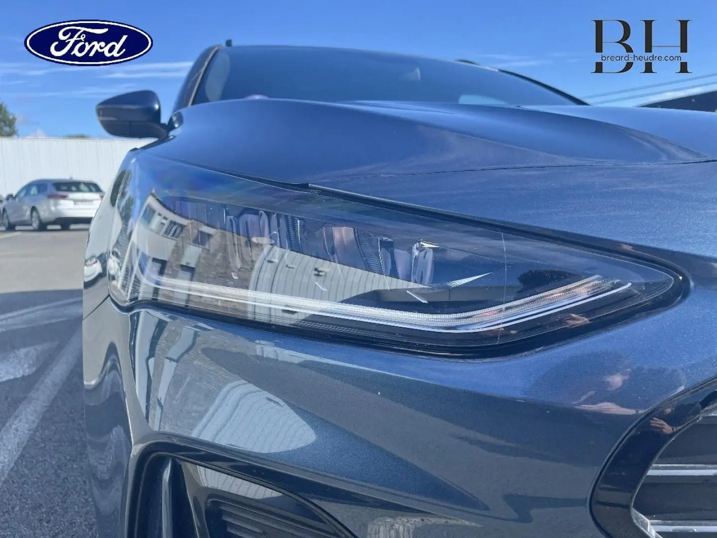 Gros plan sur le phare avant gauche bleu azur métallisé de la Ford Focus SW 2024, soulignant ses lignes modernes et épurées.