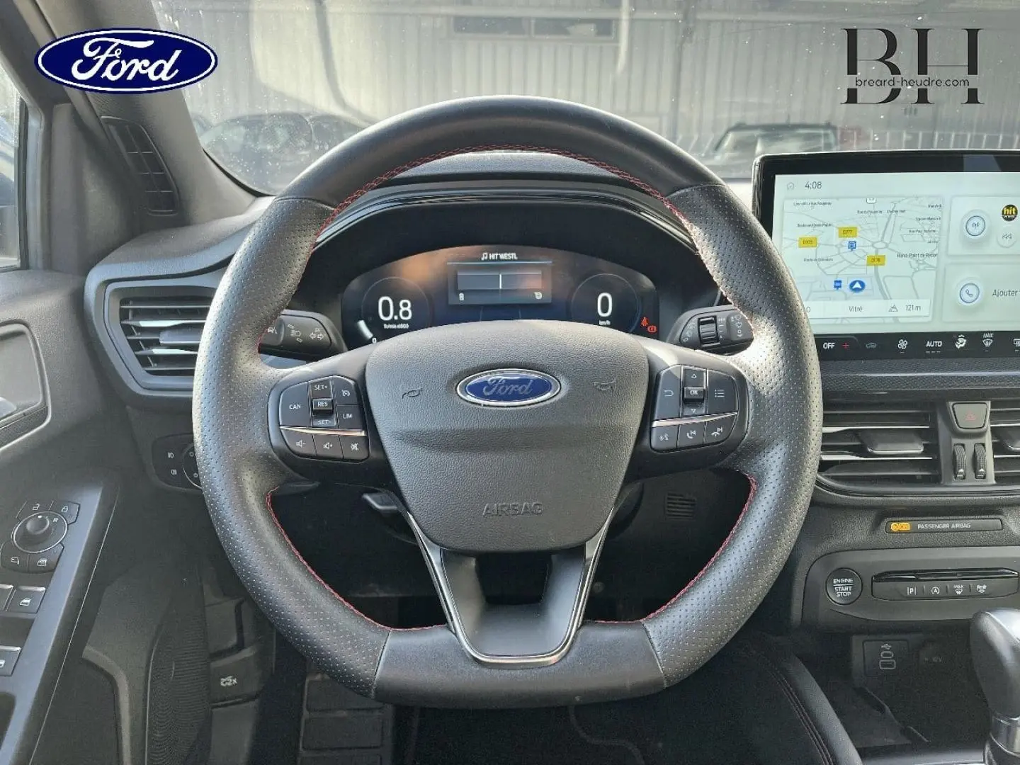 Vue centrée sur le volant cuir perforé avec surpiqûres rouges et tableau de bord numérique de la Ford Focus SW 2024.