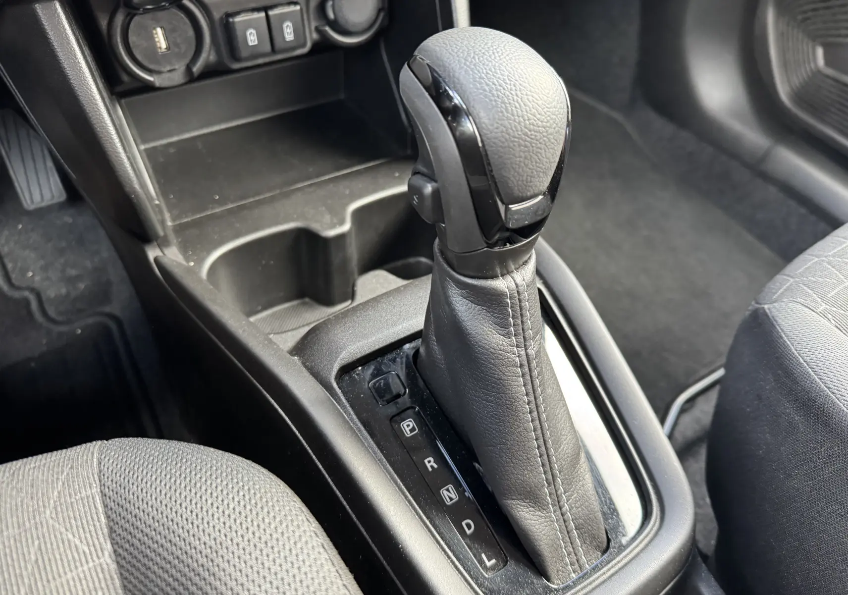 Gros plan sur le levier de vitesse automatique noir et gris de la Suzuki Swift 1.2 Hybrid Privilege 2025, intérieur sombre.