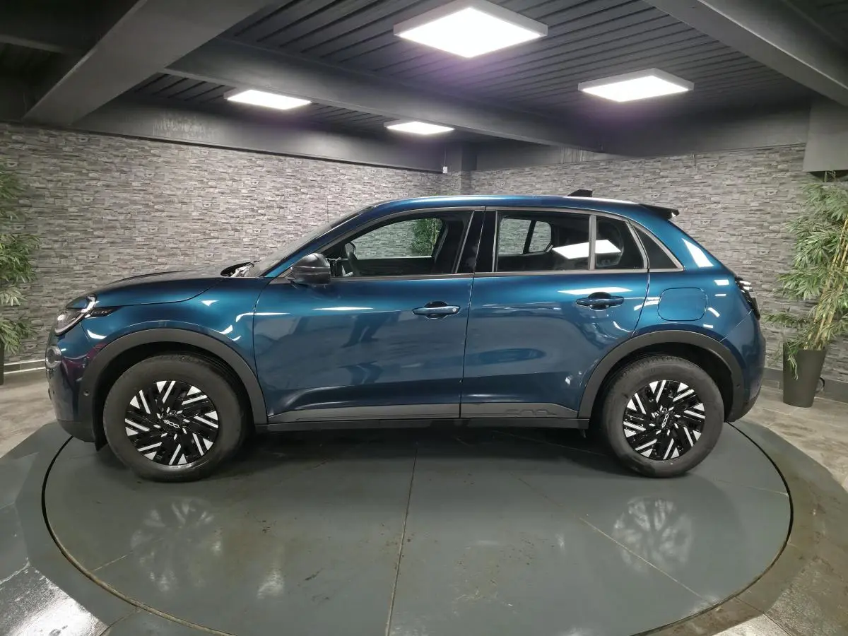 Vue de profil côté gauche d'une FIAT 600 1.2 Hybrid 2024 bleu métallisé avec jantes bicolores et coques de rétroviseurs noires.