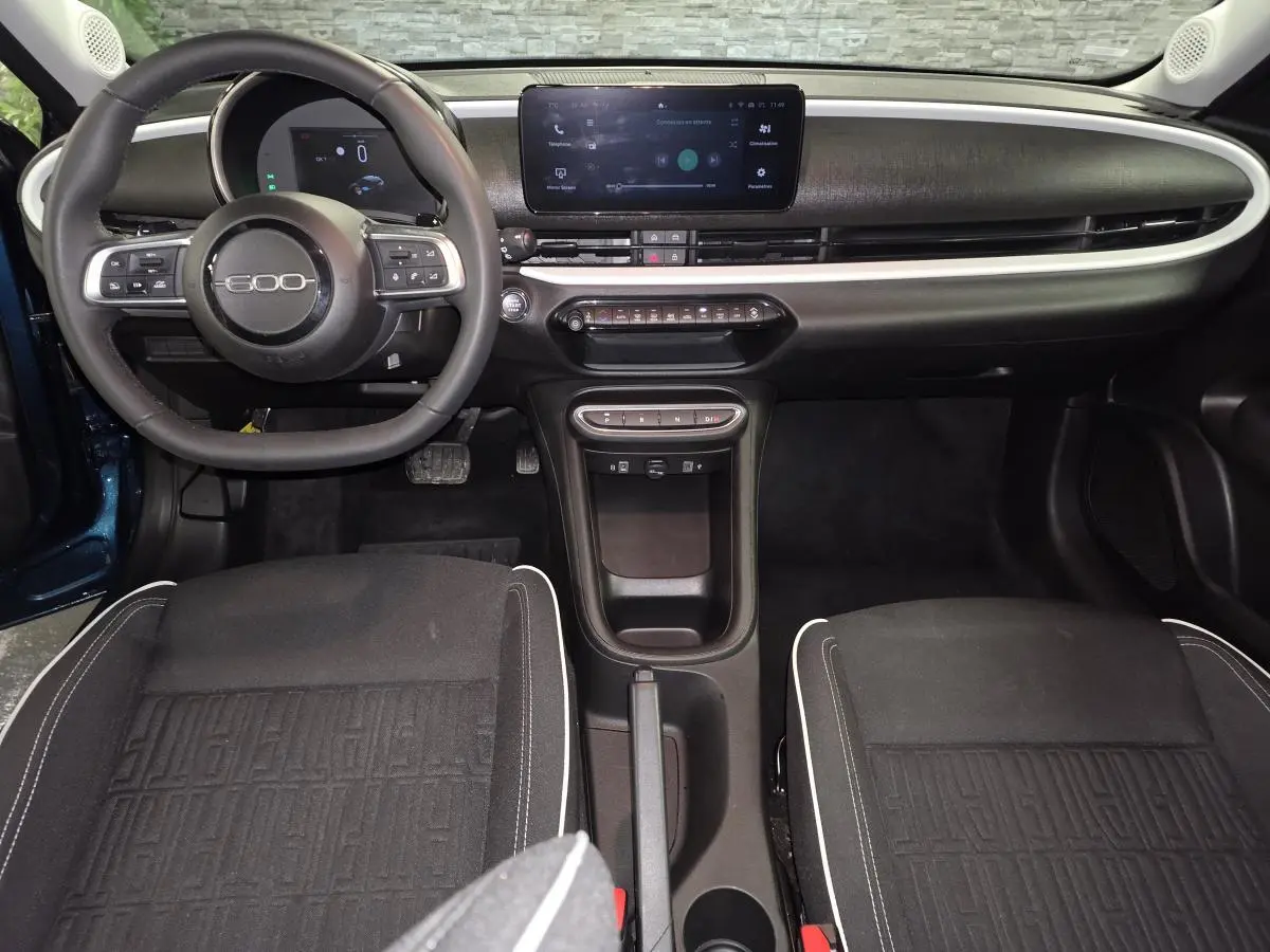 Vue intérieure avant de la FIAT 600 Hybrid 2024 avec tableau de bord noir mat et écran tactile central.