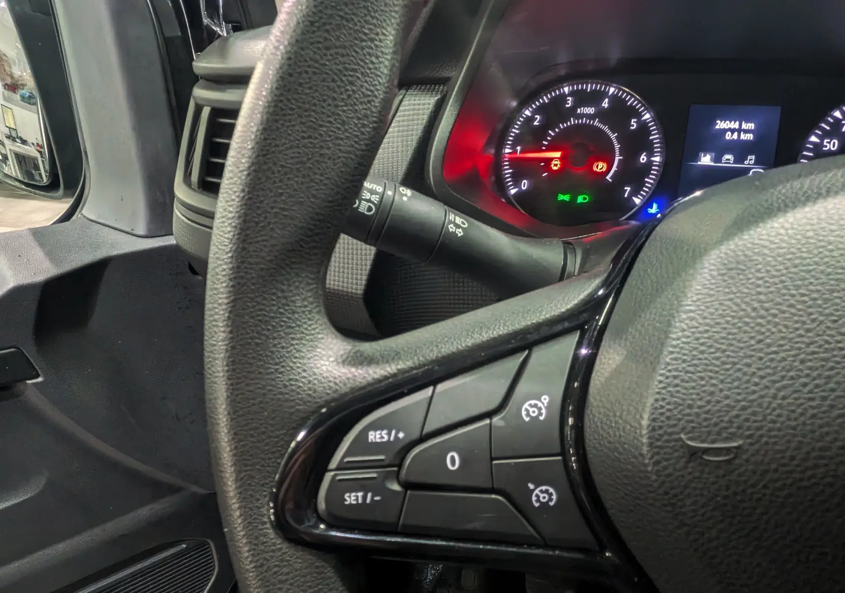 Gros plan sur le volant côté gauche du Renault Trafic Combi gris, avec commandes de régulateur de vitesse et tableau de bord lumineux.