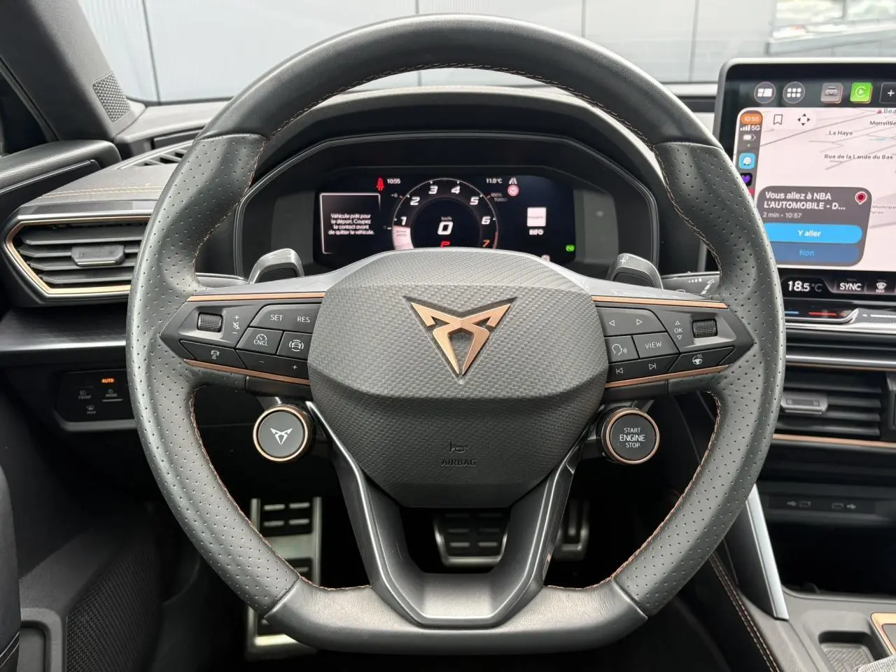 Vue rapprochée du volant cuir perforé noir avec logo CUPRA cuivré et tableau de bord digital d'une Leon 2025.