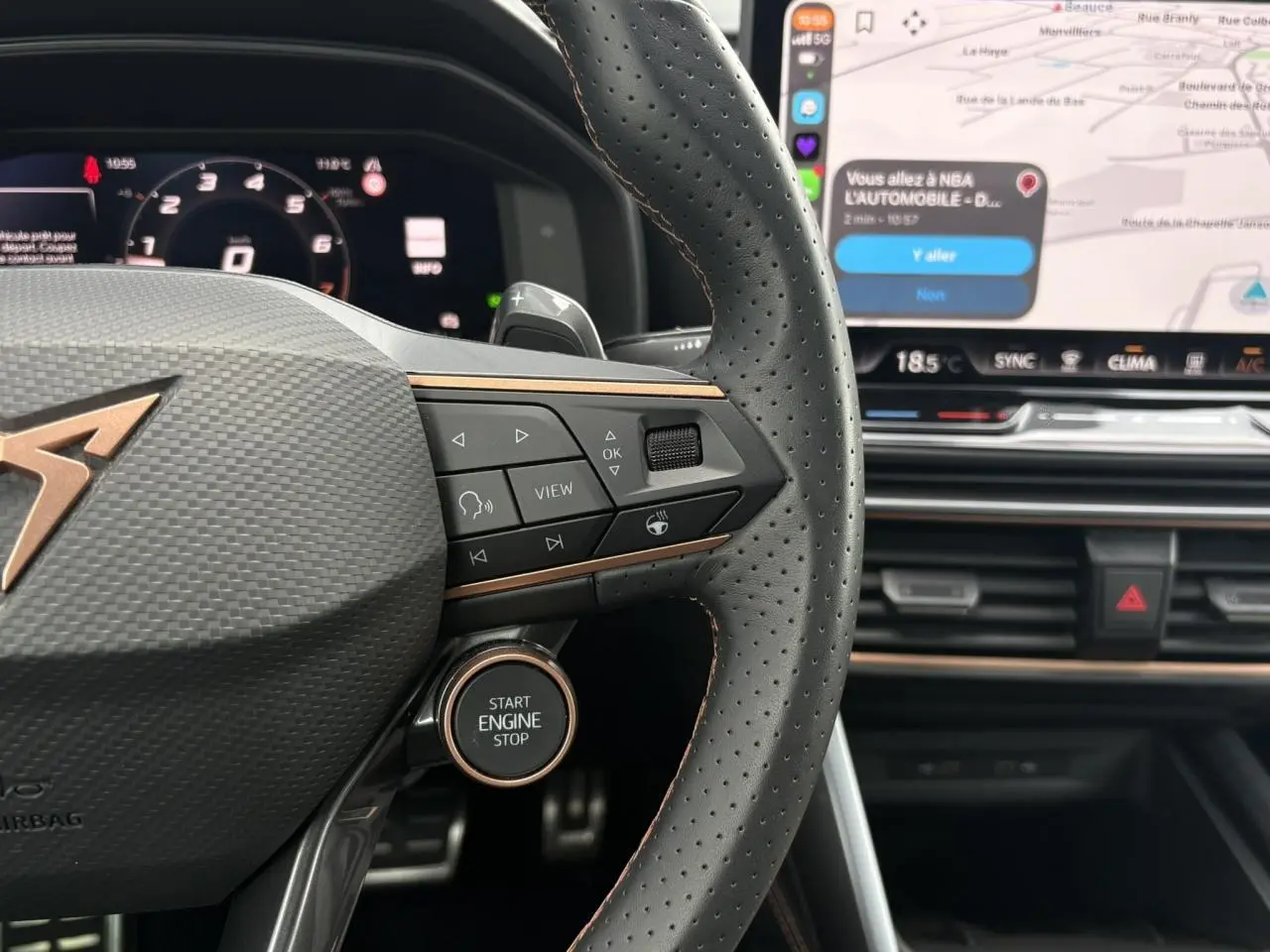 Gros plan sur le volant perforé noir avec logo CUPRA cuivré et bouton Start Engine, tableau de bord digital et écran tactile visible.