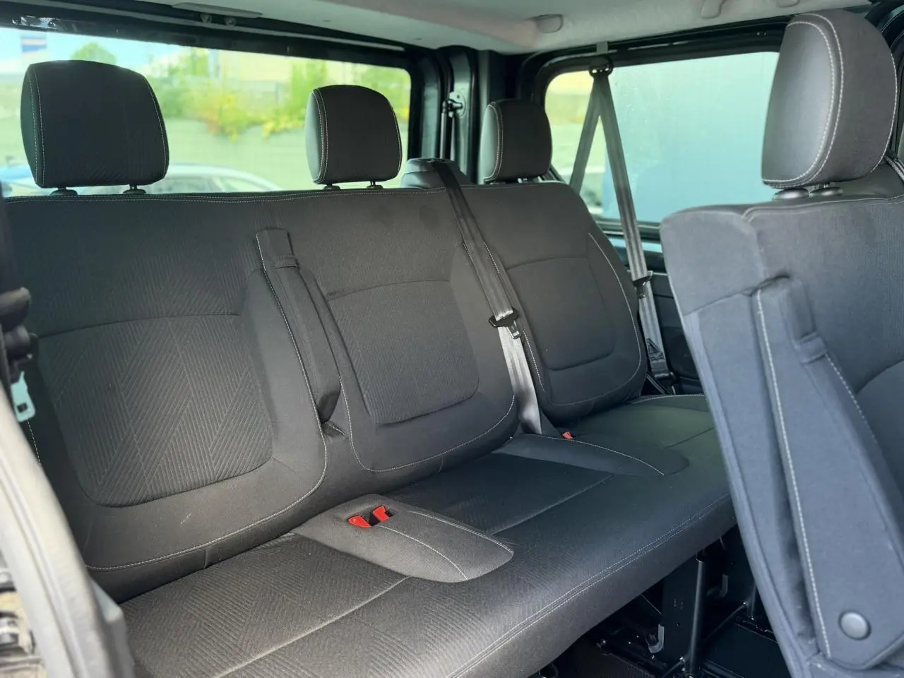 Vue intérieure sur la deuxième rangée de sièges noirs du Nissan Primastar Combi gris, avec ceintures et appuie-têtes visibles.