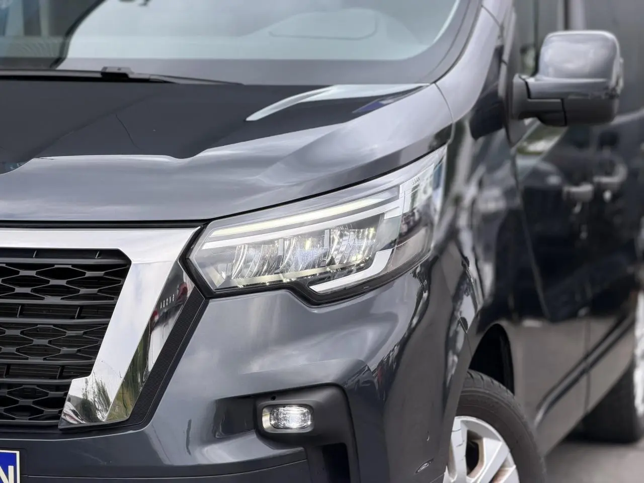 Vue 3/4 avant droit du Nissan Primastar Combi gris Comète, mettant en valeur ses phares LED et la calandre chromée.