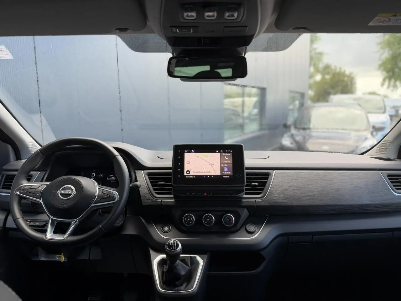Vue intérieure frontale du tableau de bord gris du Nissan Primastar Combi avec écran tactile et volant multifonctions.