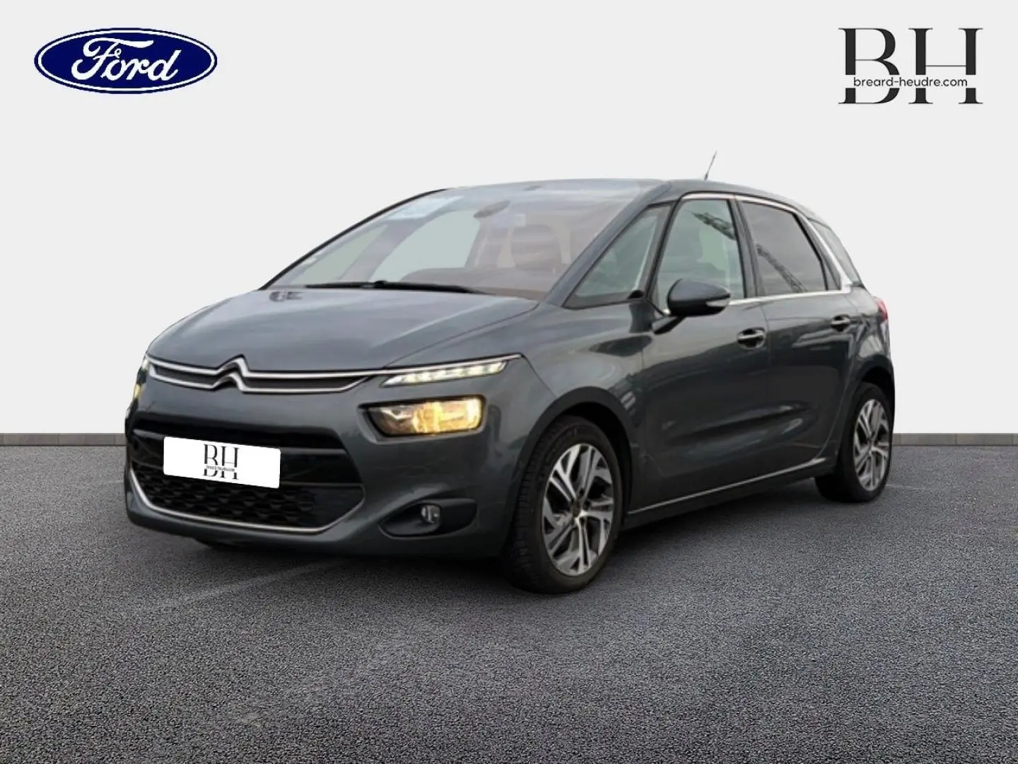 Citroën C4 Picasso gris Shark vue 3/4 avant droit avec phares allumés sur fond neutre.