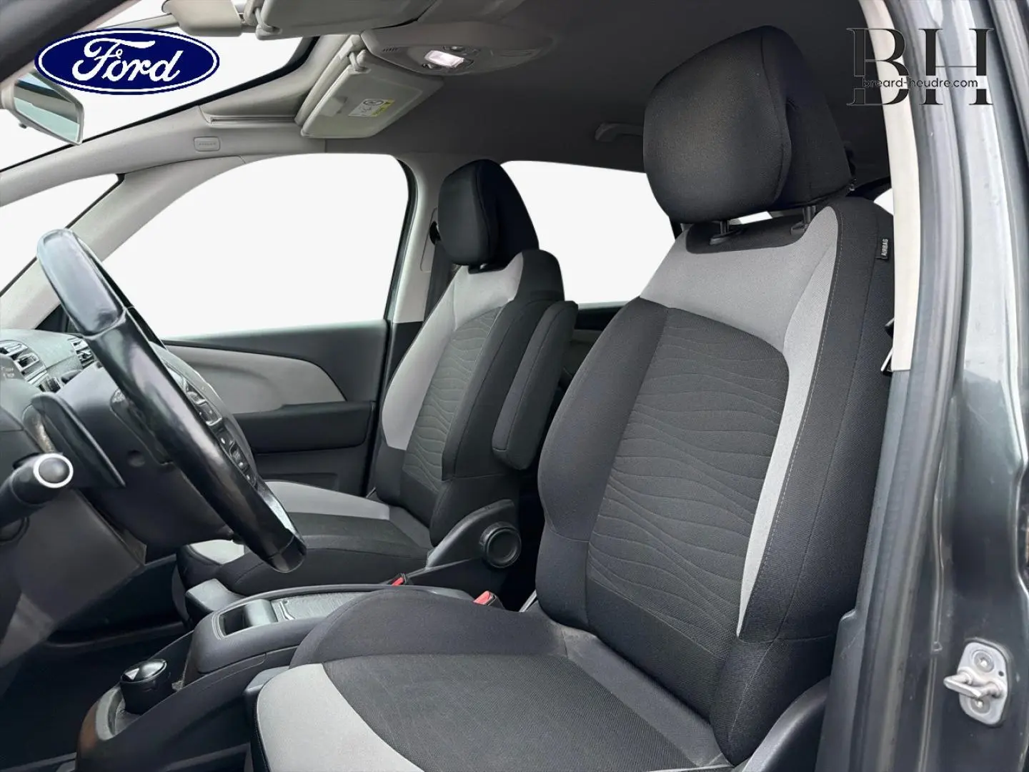 Vue intérieure côté conducteur de la Citroën C4 Picasso gris Shark, montrant les sièges avant en tissu bicolore noir et gris.