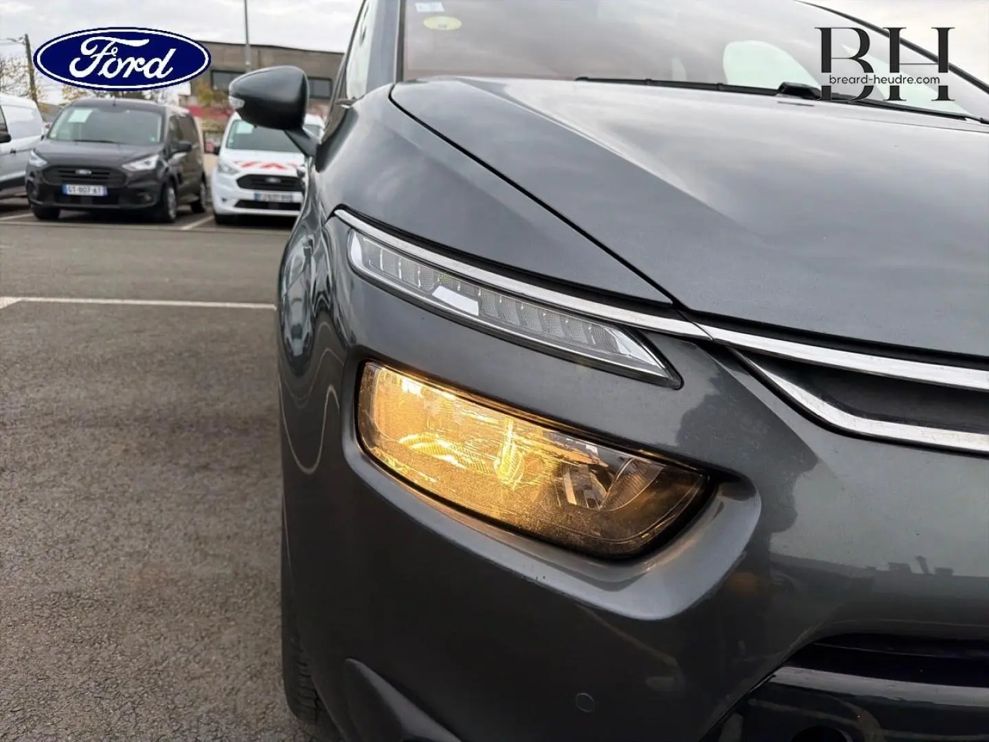 Gros plan sur l'avant droit gris Shark d'une Citroën C4 Picasso 2016 avec feu de jour LED et clignotant allumé.