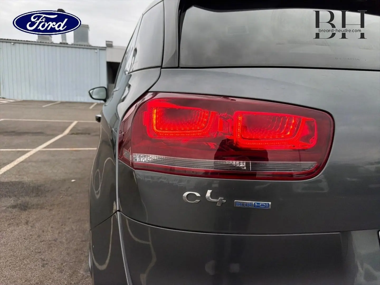 Gros plan sur le feu arrière droit d'une Citroën C4 Picasso gris Shark avec logo C4 et badge BlueHDi visible.