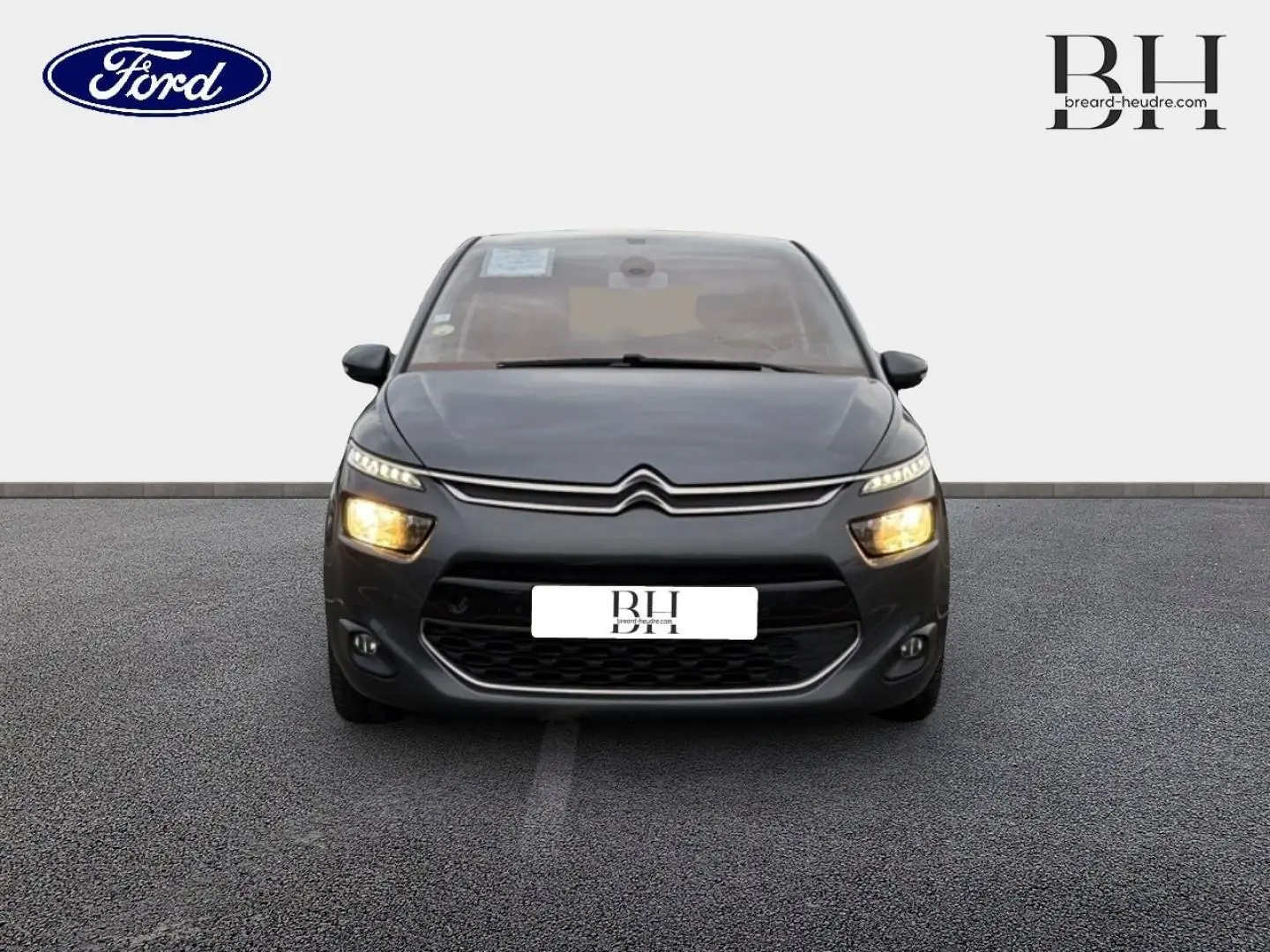Vue de face d'une Citroën C4 Picasso gris Shark avec feux allumés sur un sol gris uniforme.
