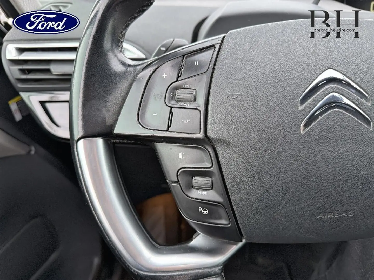 Gros plan sur le volant cuir gris avec commandes multifonctions et logo Citroën au centre, intérieur sombre.
