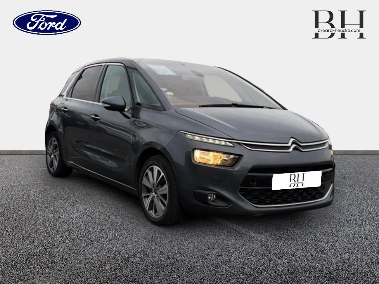 Citroën C4 Picasso gris Shark vue 3/4 avant droit avec feux allumés sur fond neutre.