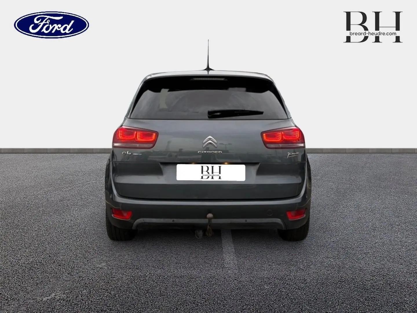 Vue arrière d'une Citroën C4 Picasso gris Shark avec feux allumés et attelage visible.